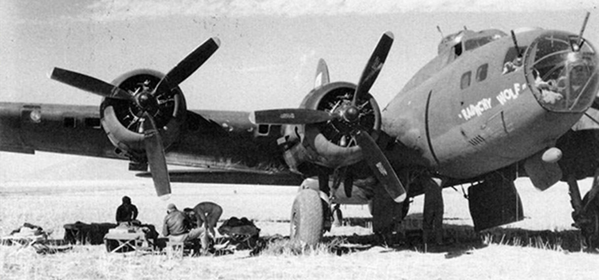 Archival black and white photograph of a WWII bomber aircraft on an airfield with ground crew nearby