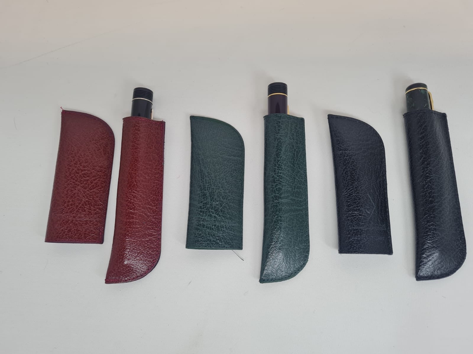 Drei erweiterbare Leder-Stiftetuis in Bordeauxrot, Grün und Marineblau, jeweils mit einem Stift