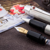 Pluma estilográfica de boda plateada con patrón de grano de cebada y joya de cabujón de rubí, apoyada junto a fotografías de boda