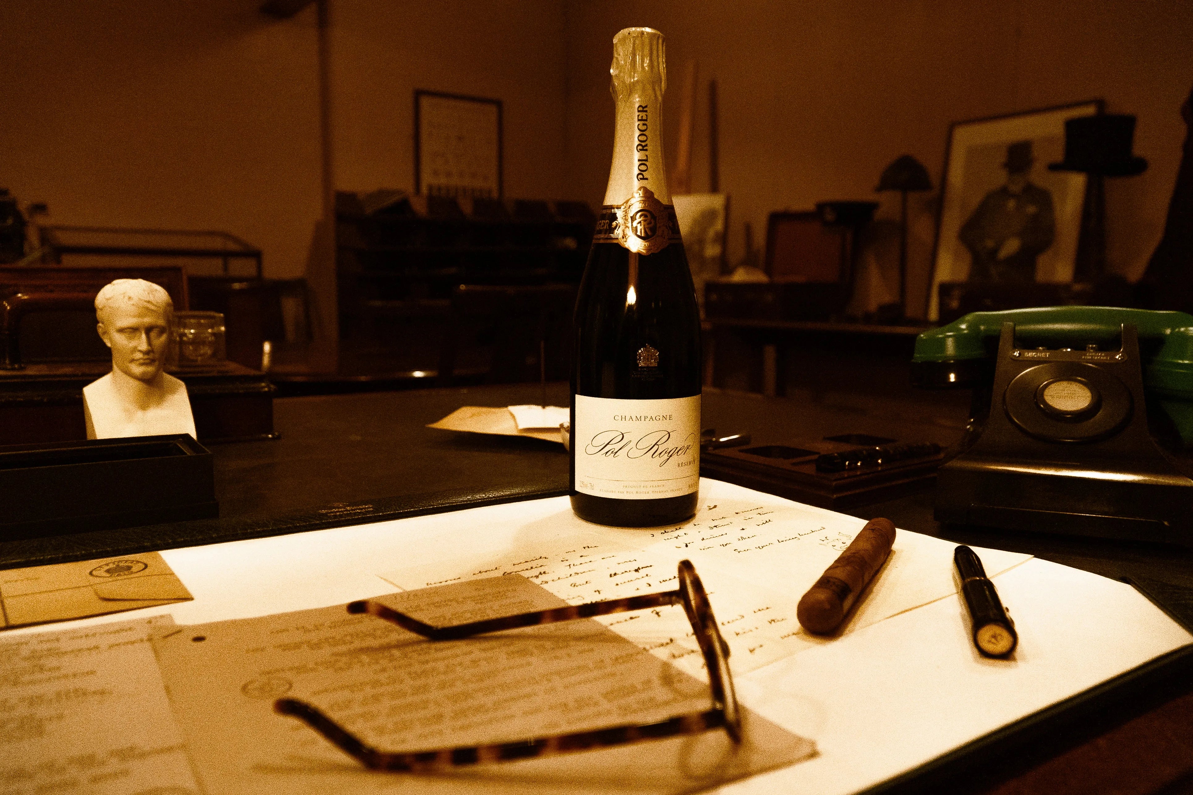 The Pol Roger 175th Anniversary fountain pen on a desk with a Pol Roger champagne bottle, cigar, and bust