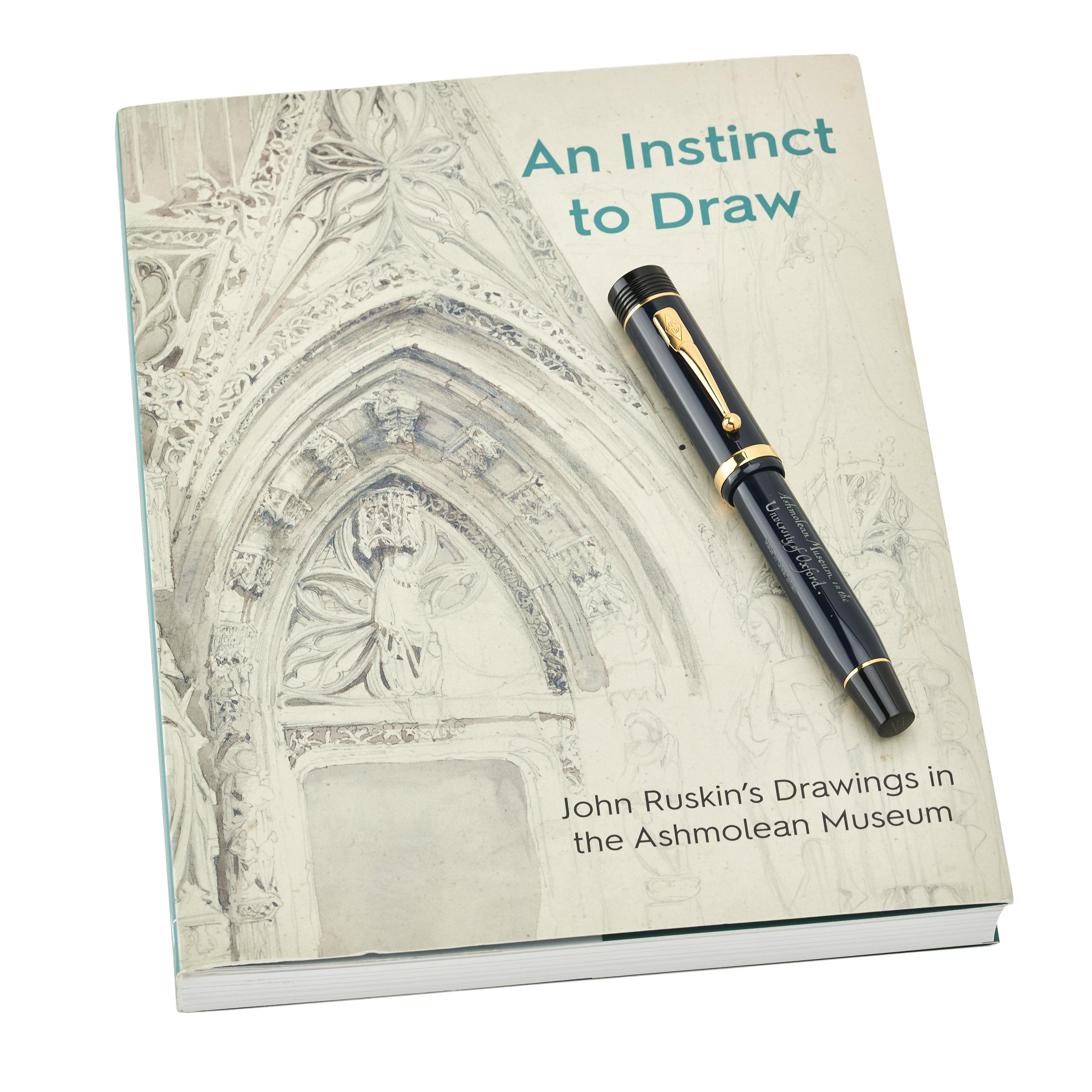 Ashmolean John Ruskin फाउंटेन पेन, An Instinct to Draw नामक पुस्तक पर रखा हुआ, जिसमें Ruskin के चित्र हैं