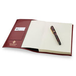 Conway Stewart luxury notebook open, showing burgundy leather cover with card slot and blank pages, pen resting on top