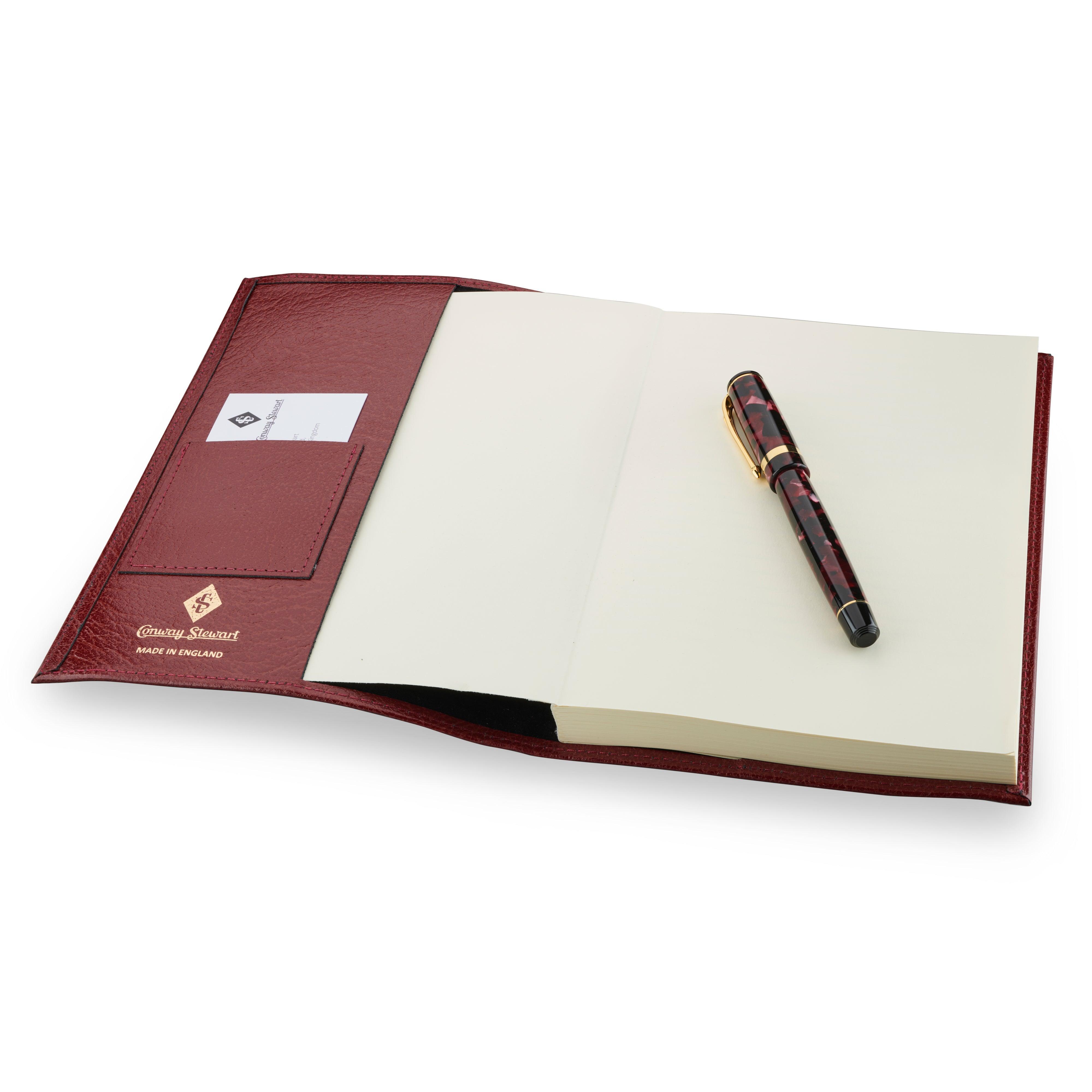 Conway Stewart luxury notebook open, showing burgundy leather cover with card slot and blank pages, pen resting on top