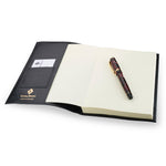 Black leather Conway Stewart notebook open, showing the card pocket, blank pages and a marbled pen on top