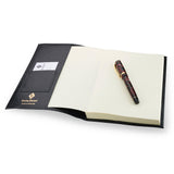 Black leather Conway Stewart notebook open, showing the card pocket, blank pages and a marbled pen on top