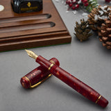 Winston Cherry Red Füllfederhalter geöffnet auf hölzerner Stiftablage, mit Tintenflasche und Tannenzapfen, festlich arrangiert