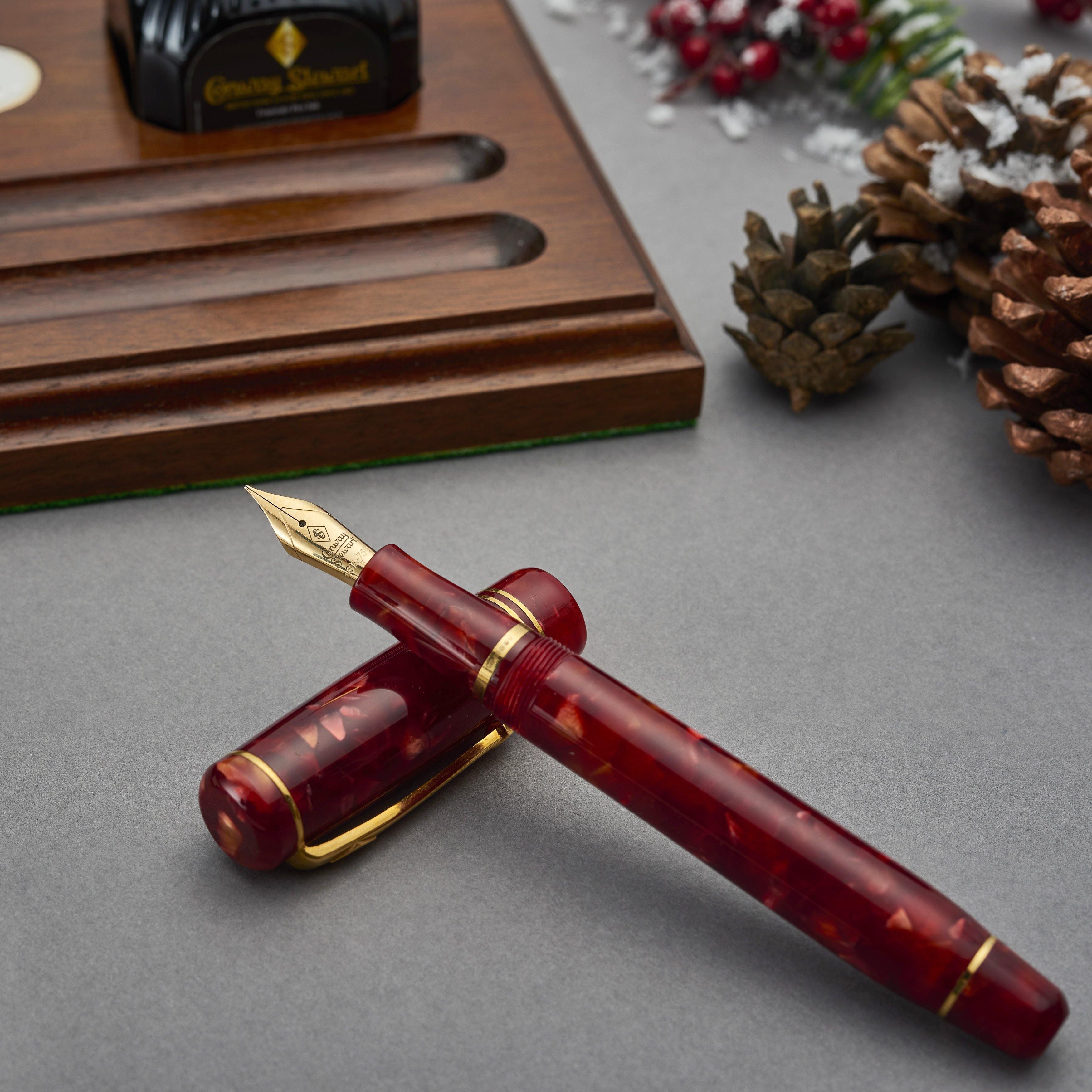 Winston Cherry Red fountain pen uncapped on a wooden pen tray, with ink bottle and pine cones in a festive display