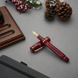 Winston Cherry Red Füllfederhalter auf einem Schreibtisch neben einem Whiskyglas und einer Armbanduhr, festlich arrangiert