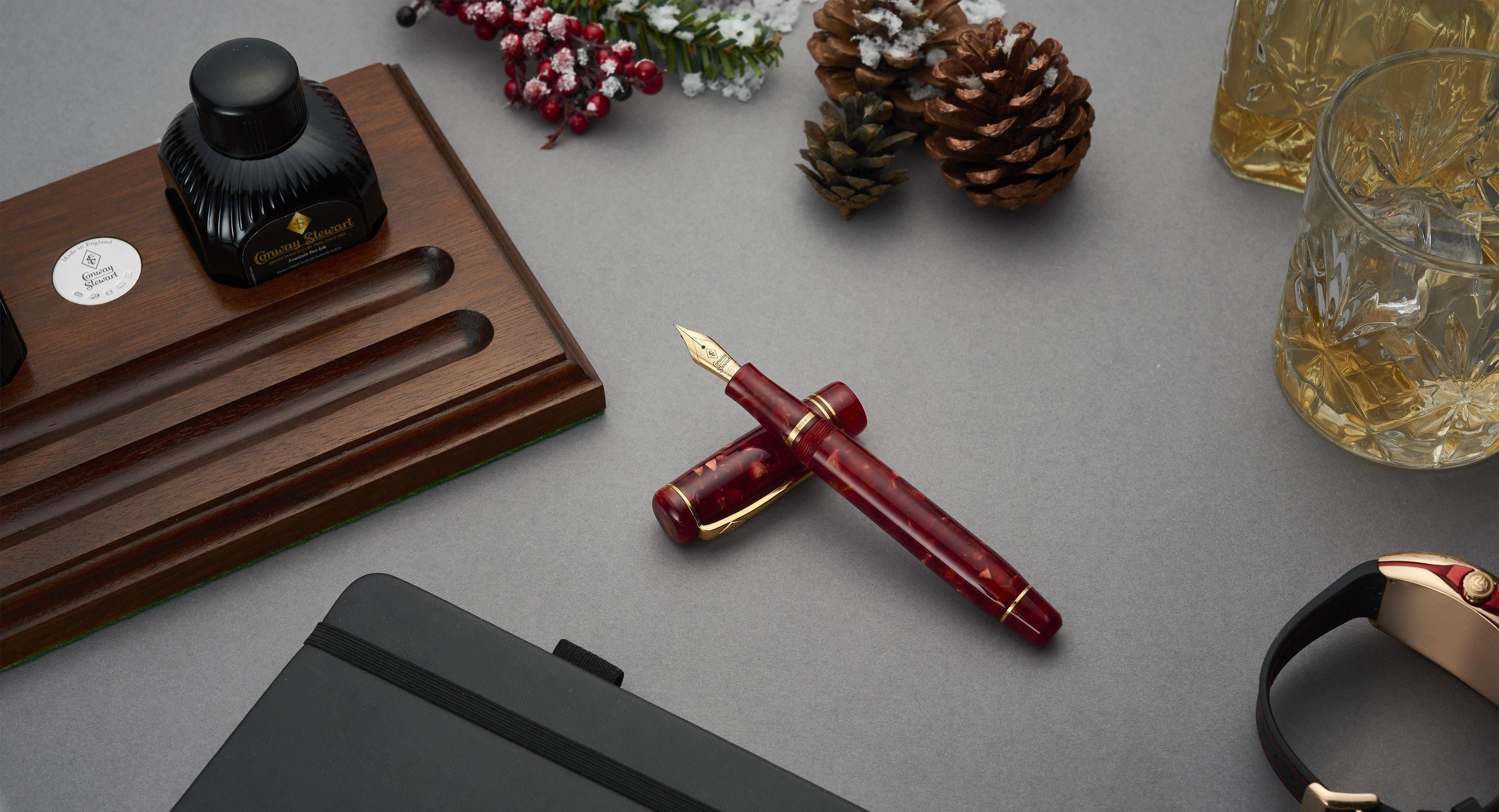 Winston Cherry Red Füllfederhalter auf einem Schreibtisch neben einem Whiskyglas und einer Armbanduhr, festlich arrangiert