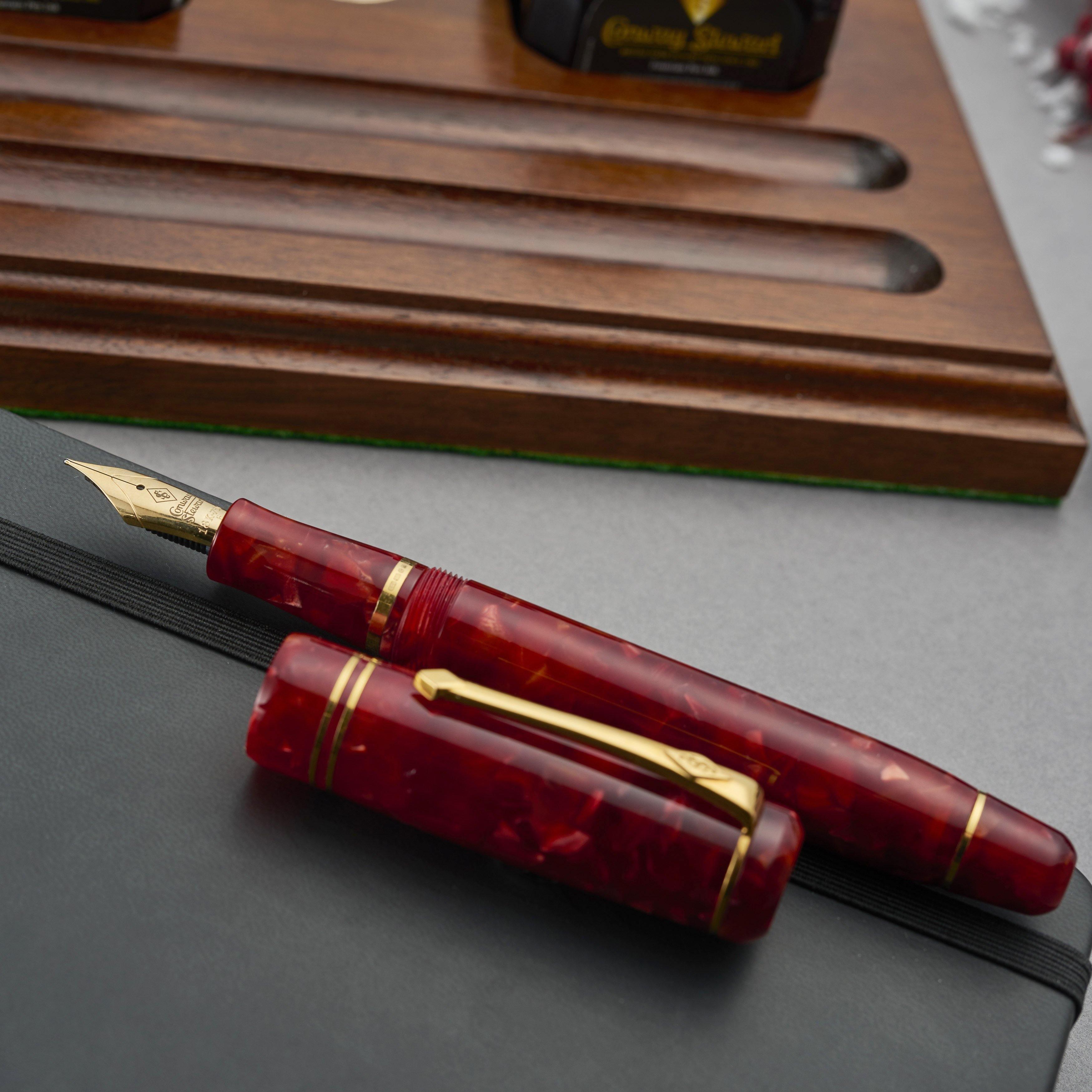 Winston Cherry Red Füllfederhalter mit Kappe über Kreuz auf einem Notizbuch, unter Stiftablage und Tintenflaschen