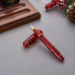 Conway Stewart Winston Cherry Red Tintenroller, Kappe quer über dem Schaft auf einem Schreibtisch, Beeren im Hintergrund
