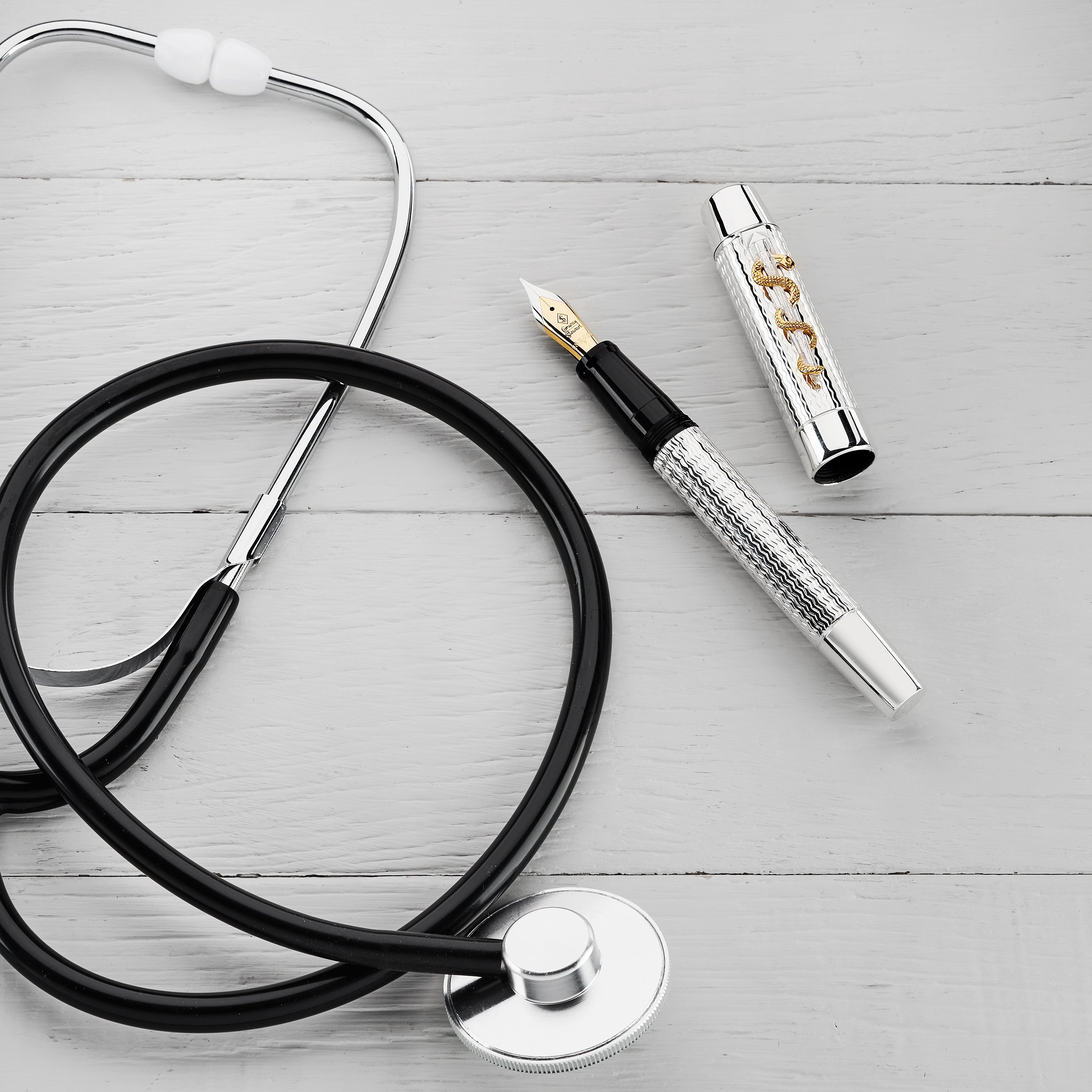 Doctor's Pen Füllfederhalter und Kappe liegen neben einem Stethoskop auf einer Holzoberfläche